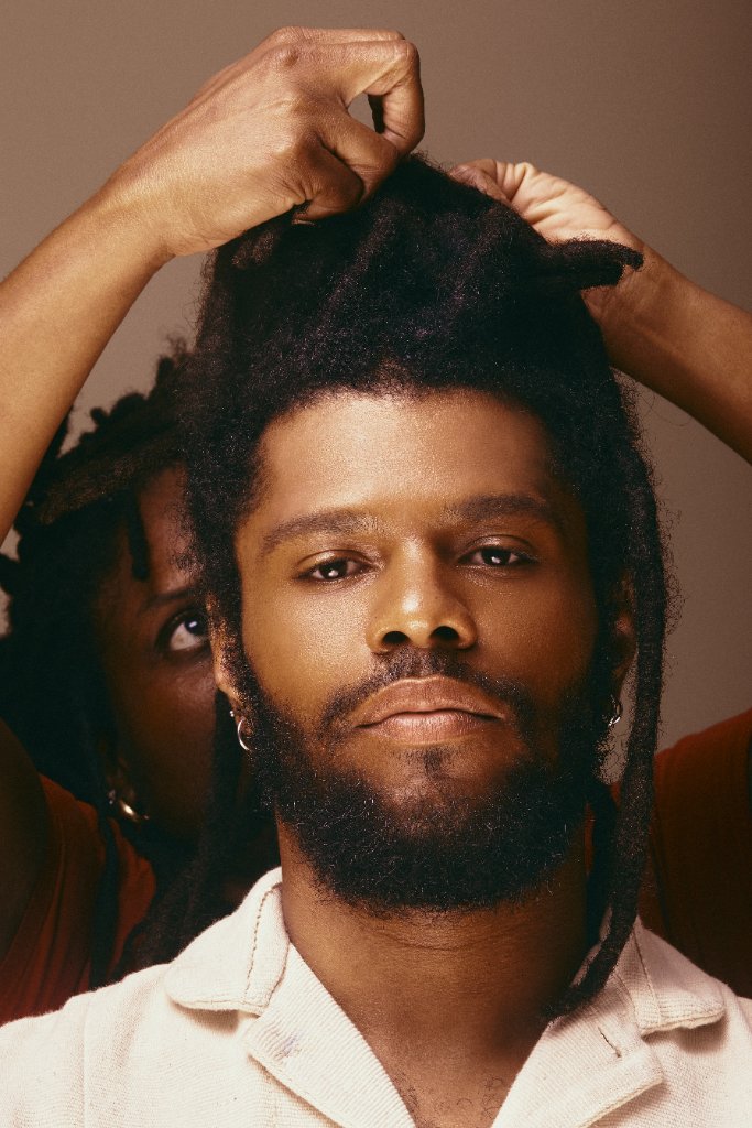Deux mains coiffent les locks d'un homme, vu de face
